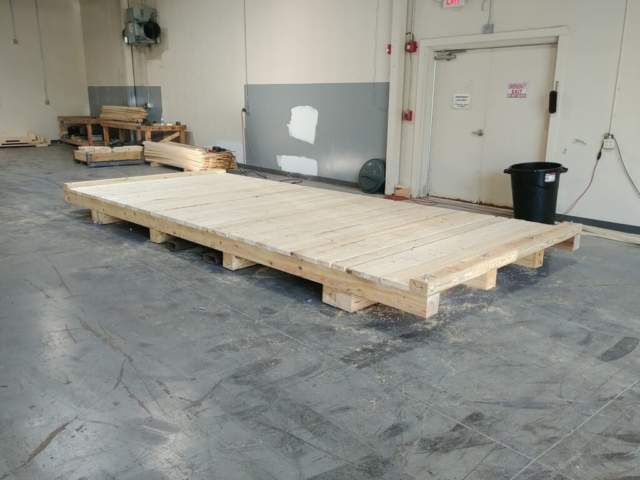 Export crates being manufactured in a workshop in Fairport, NY, with workers assembling sturdy wooden crates for international shipping. ISPM certified